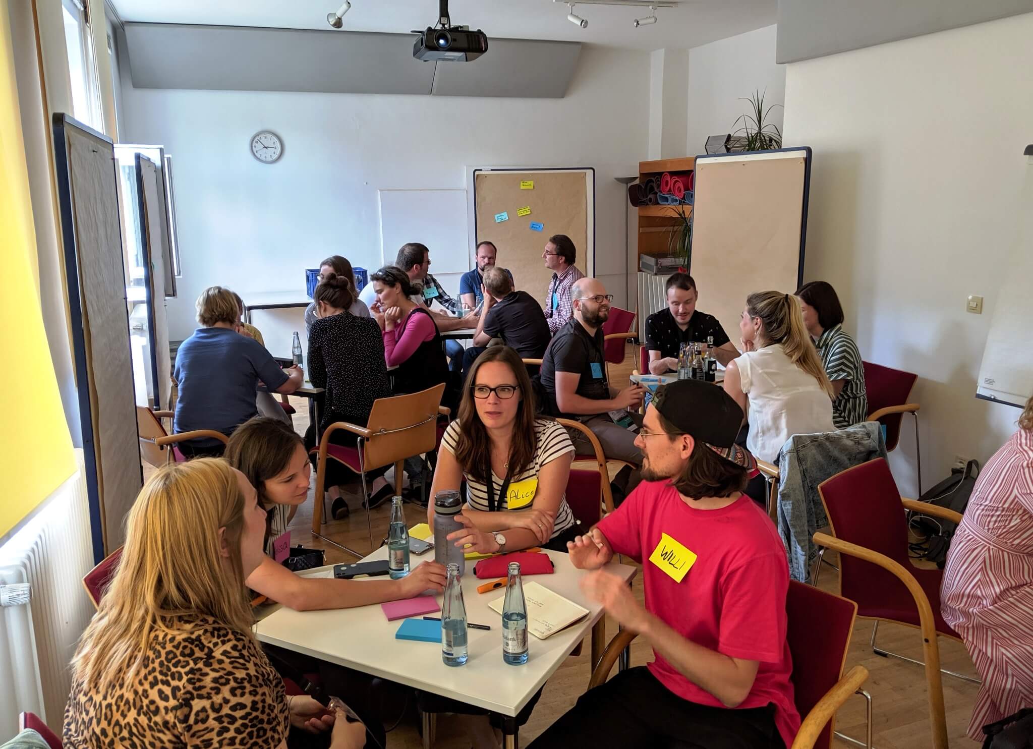 Jock Busuttil runs a product management training workshop for a room of people with name tags seated at square tables at Working Products 2019 (Photo by Jock Busuttil / Product People Limited)