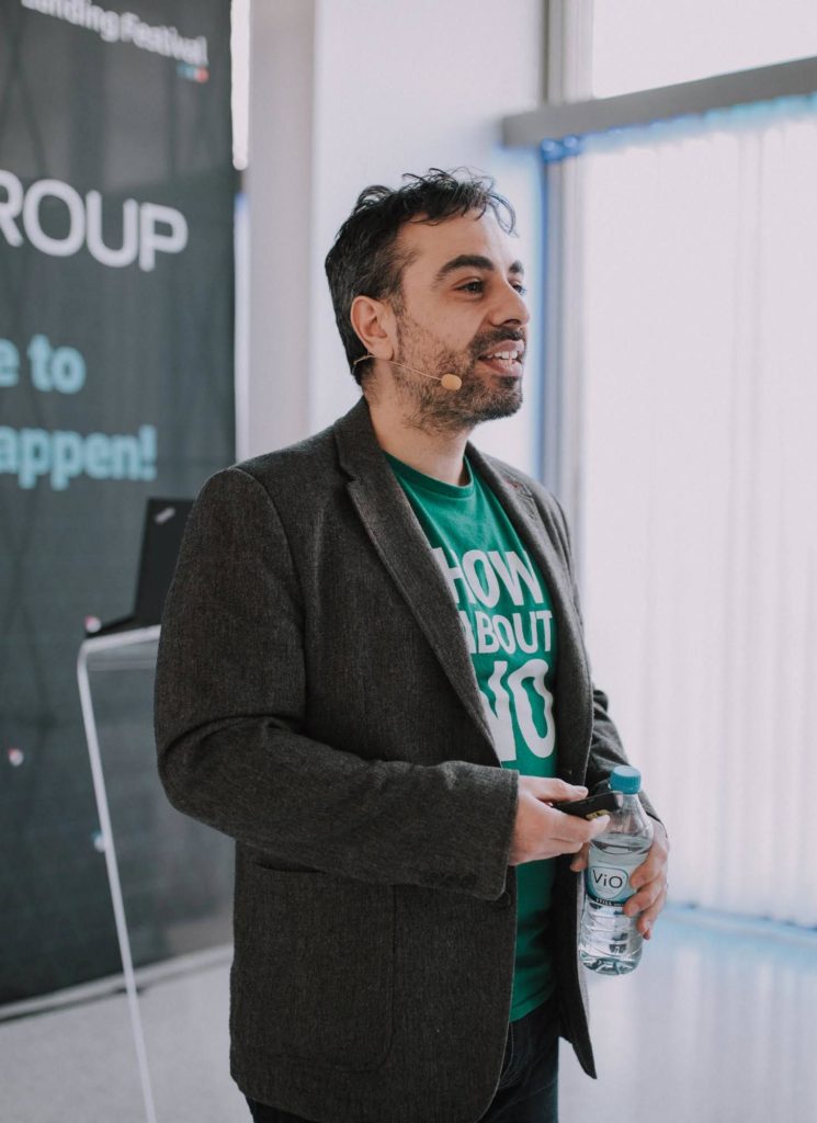 Jock Busuttil standing in profile holding a bottle of water while giving his talk "The Secrets of Meaningful Roadmaps" at Landing Festival 2019 (Photo by Landing Jobs)