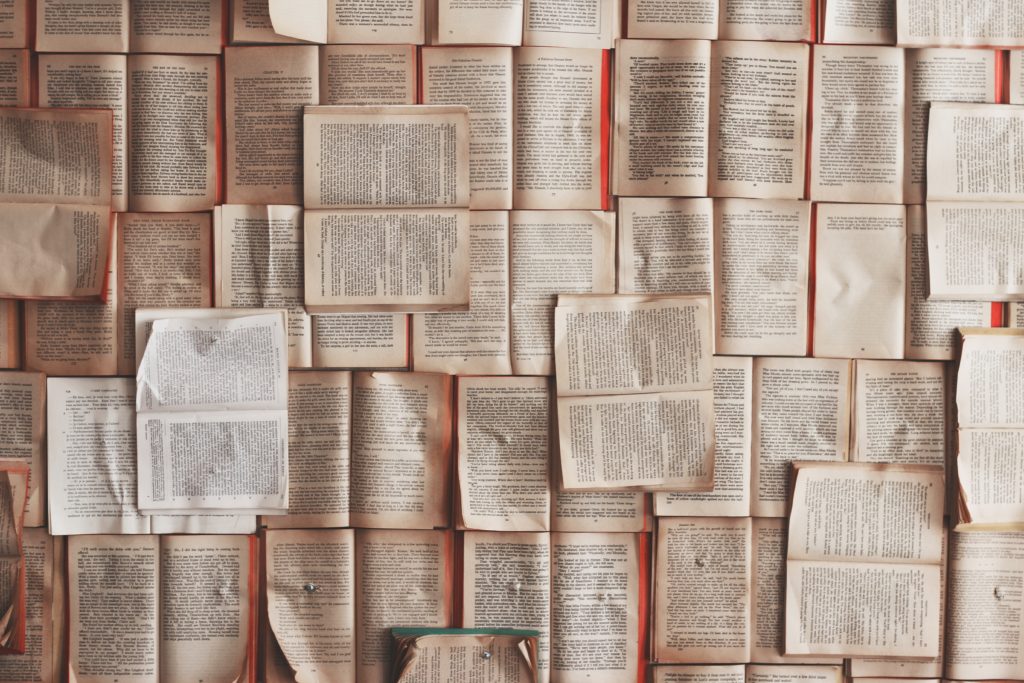 Open books are pinned to a wall like overlapping tiles (Photo by Patrick Tomasso on Unsplash)
