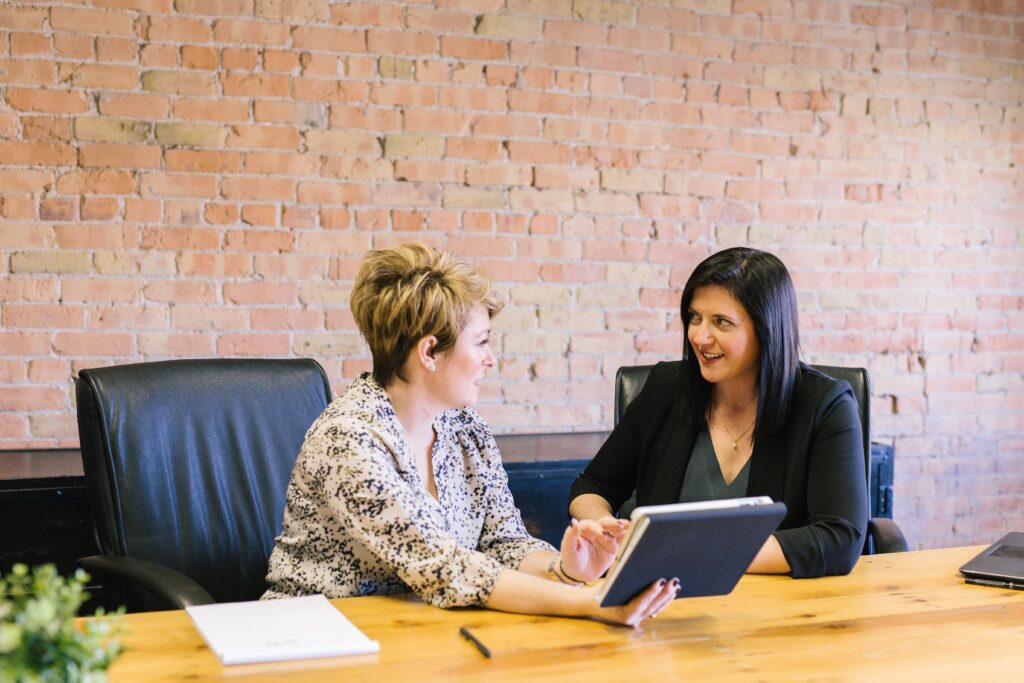 Two people chatting in front of a wall in an office. Photo by Amy Hirschi on Unsplash.